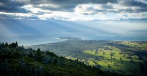 View of the sea and green fields with sun rays shining through the clouds