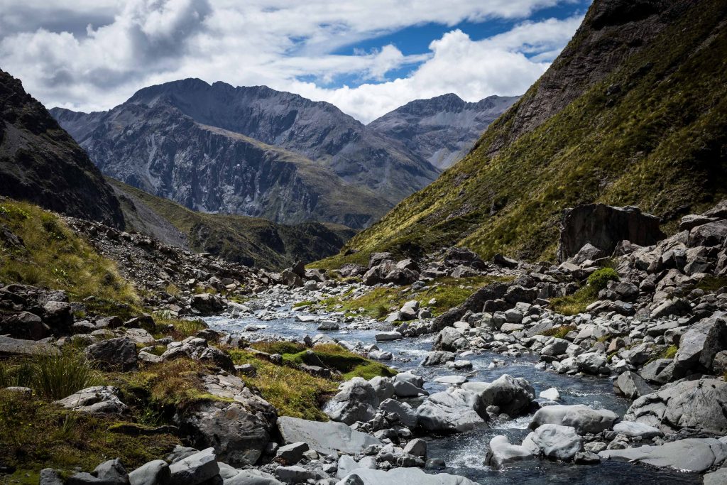 A rocky stream flowing through a valley towards mountains in the background